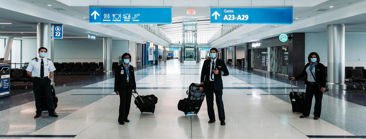 flight crew featured standing six feet apart demonstrating CODVID-19 restrictions wearing face masks and flight crew uniforms with luggage, in Concourse A