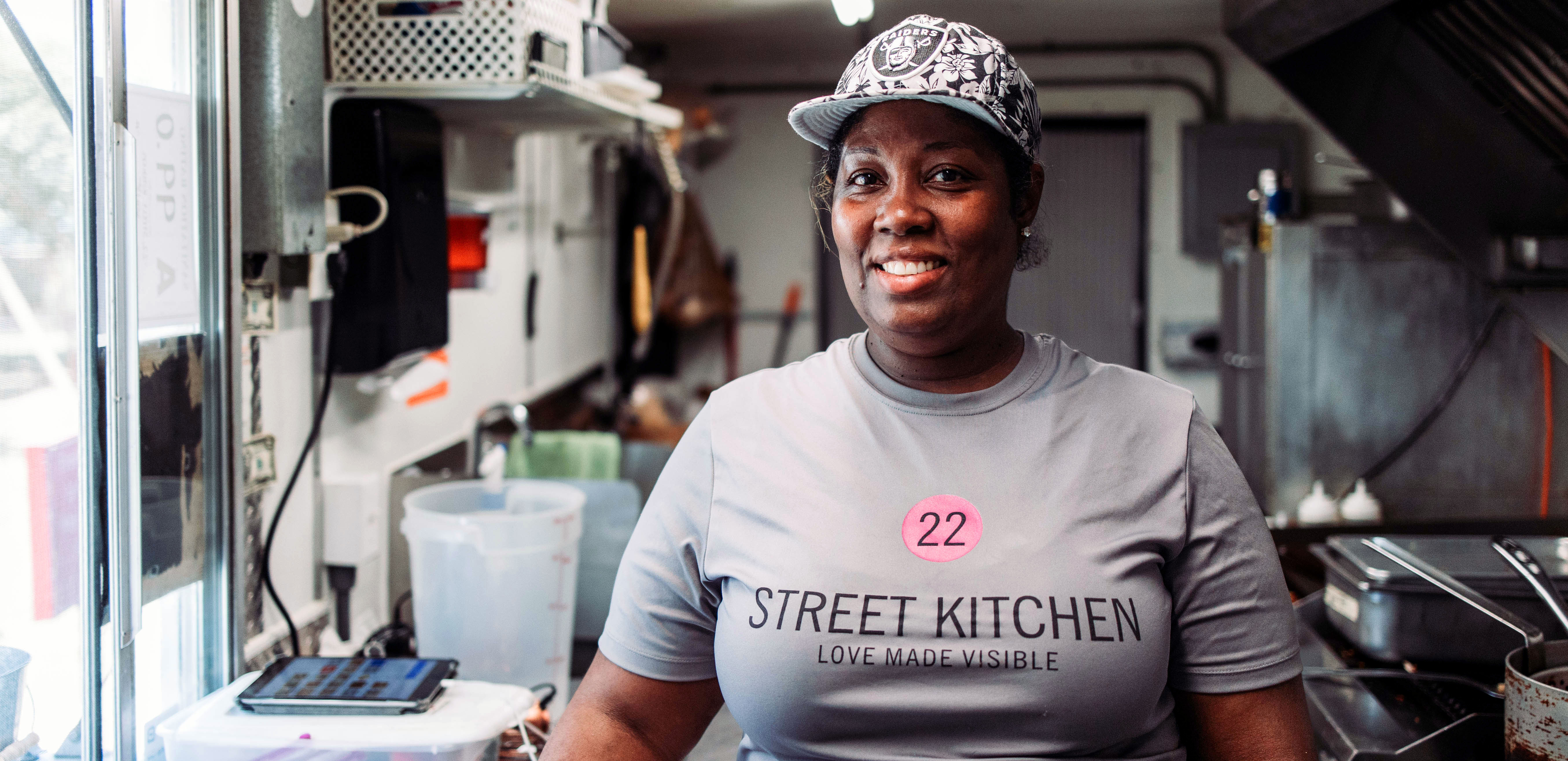 Felicia Reese owner of 22 Street Kitchen smiling big featured in her food truck, behind her is a stovetop grill and cooking appliances 