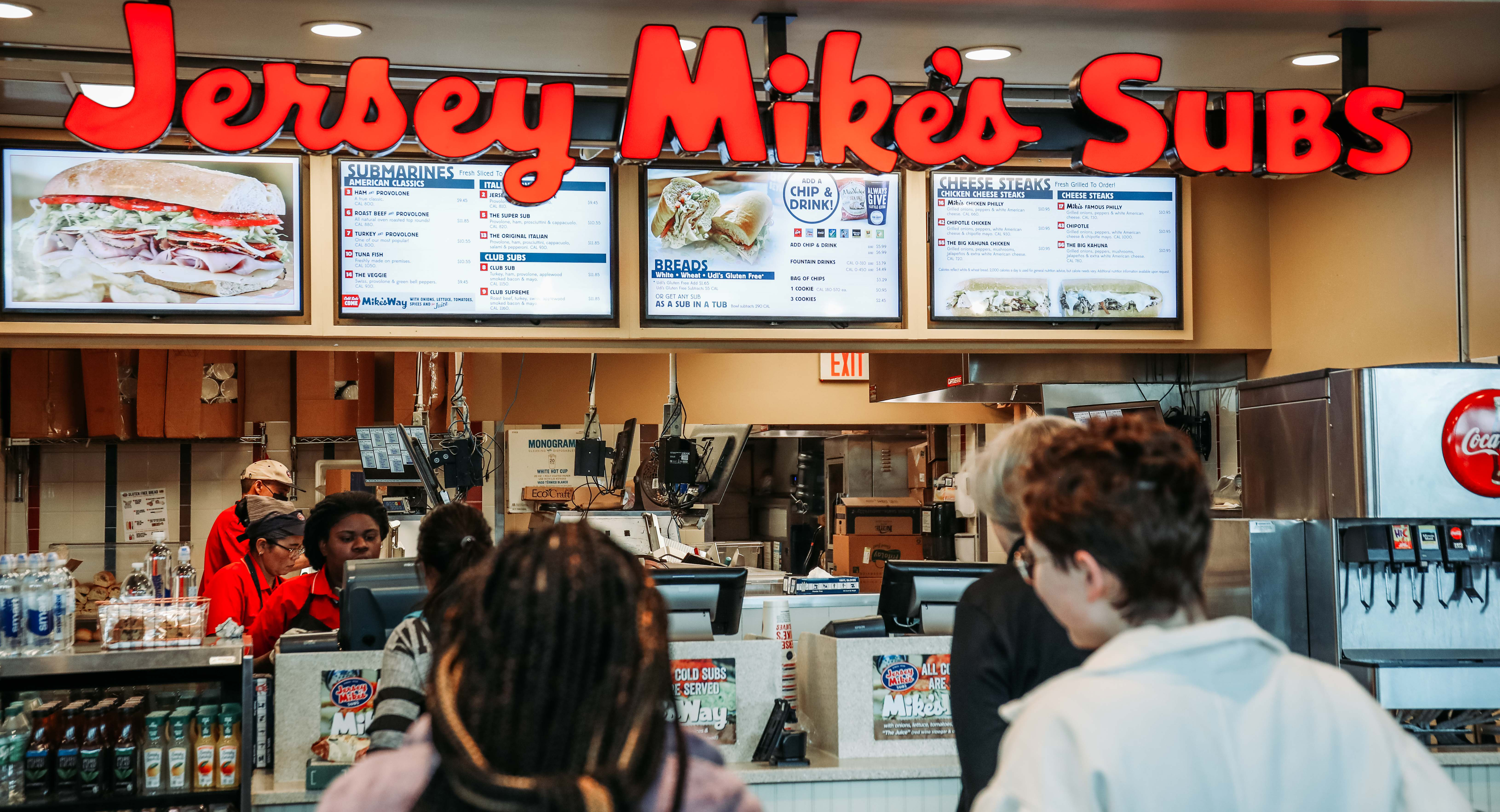 Customers stand in line at the Jersey Mike's restaurant in the Airport atrium while cashiers take and fill orders