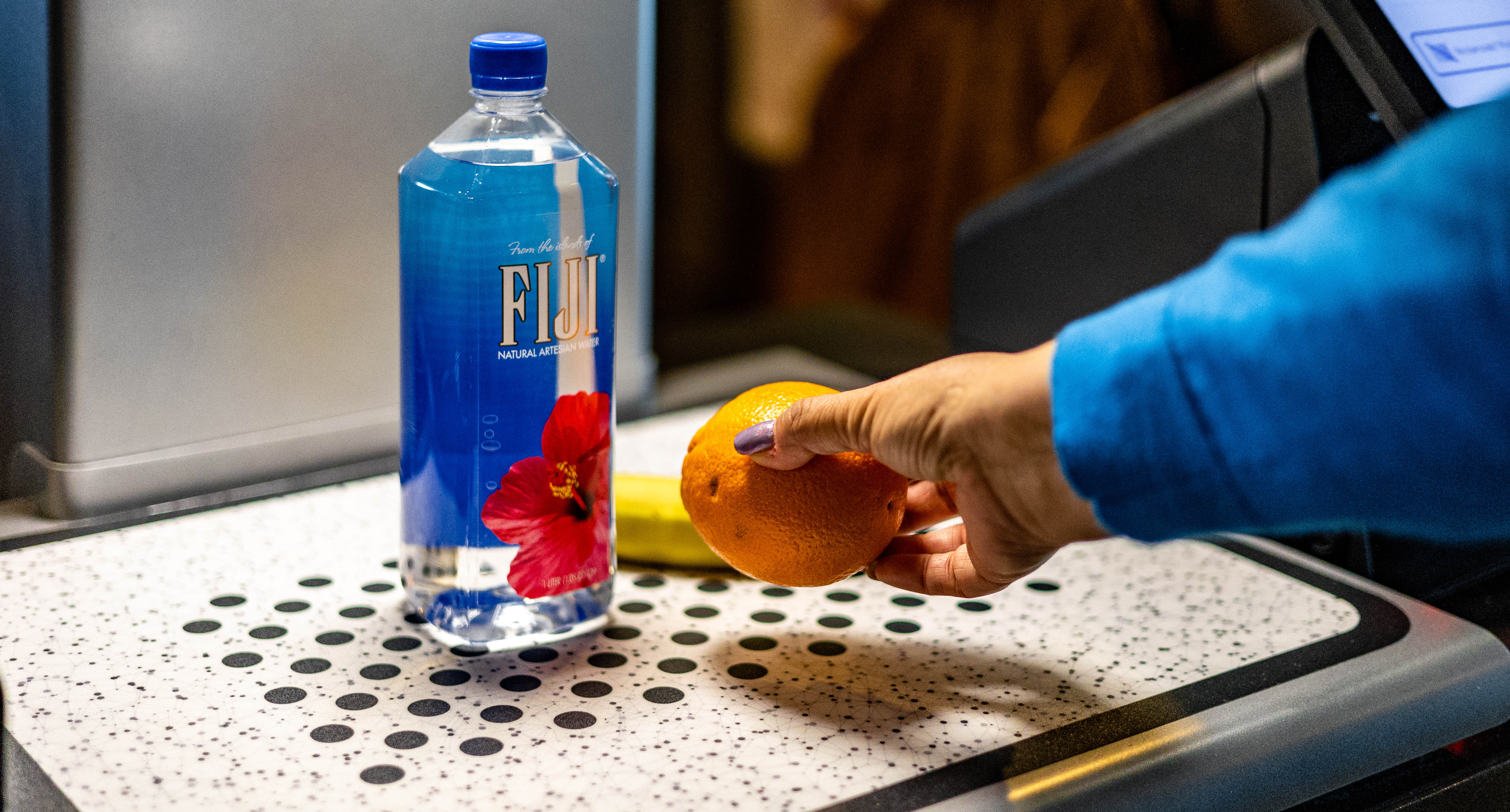 Mashgin kiosk, person holding orange with Fiji water bottle and banana
