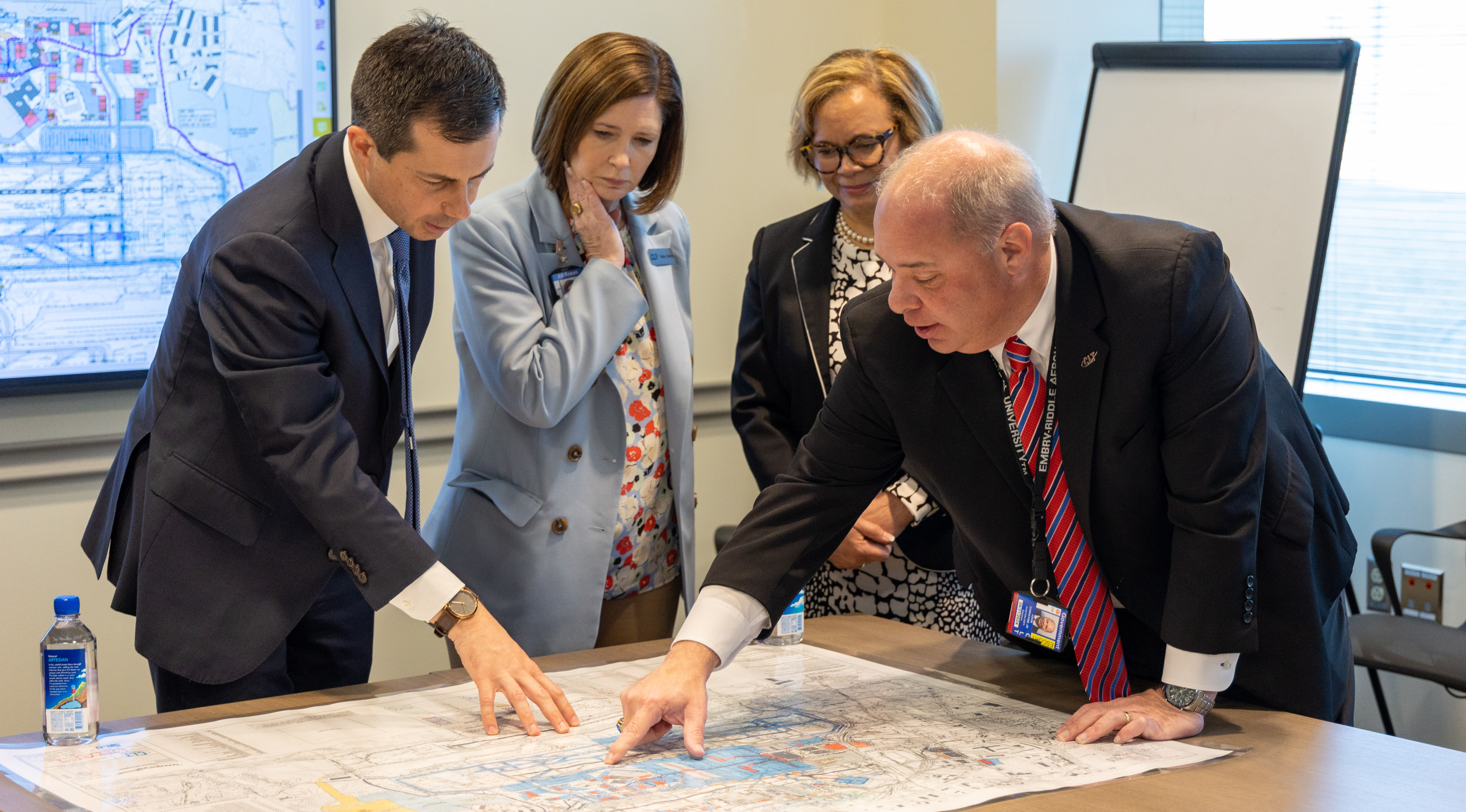 Aviation leadership team, mayor, and US Department of Transportation Secretary pointing and viewing a map of operational safety and airfield investment  