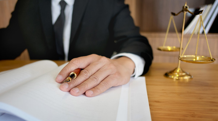 person's hand on open book holding a pen, checks and balances scale on desk next to person