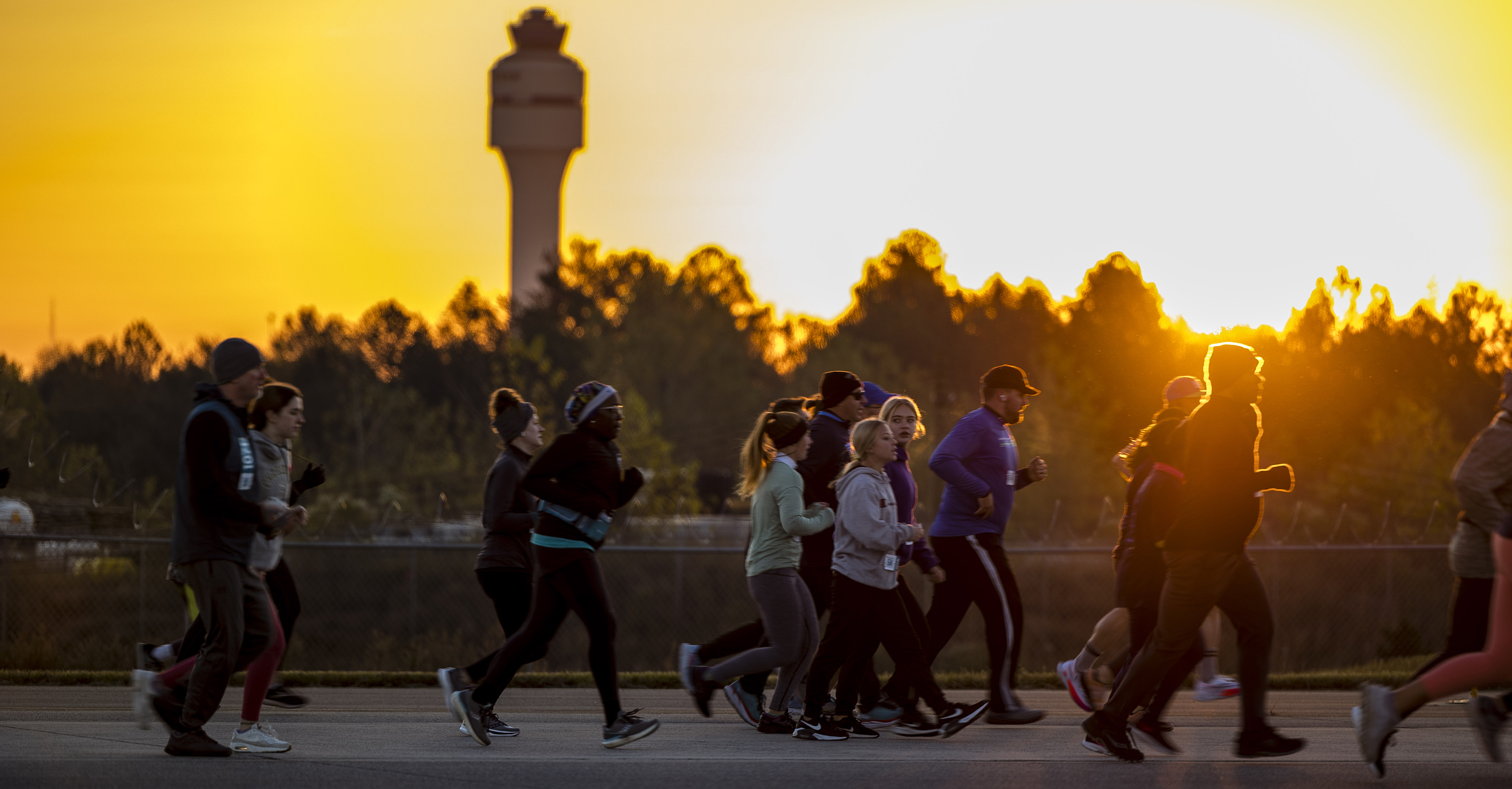Runway 5K runners running on the airfield with early morning sunrise and FAA Tower in the background and trees
