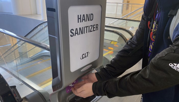 passenger featured using hand sanitizer station near escalator in CLT Terminal Lobby 